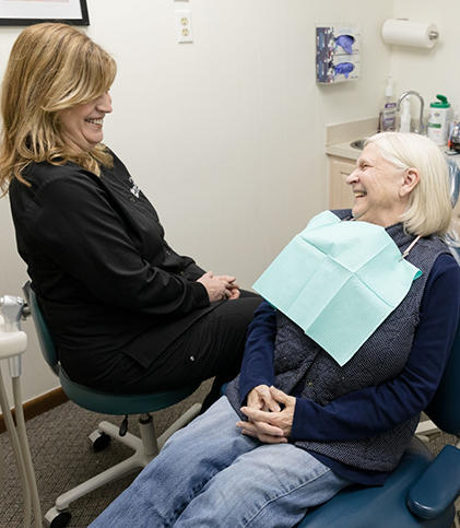 Female patient smiling and talking to female dentist while lying back in dental chair