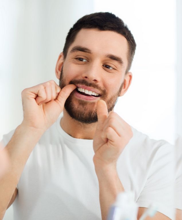 Man flossing his teeth while looking in mirror