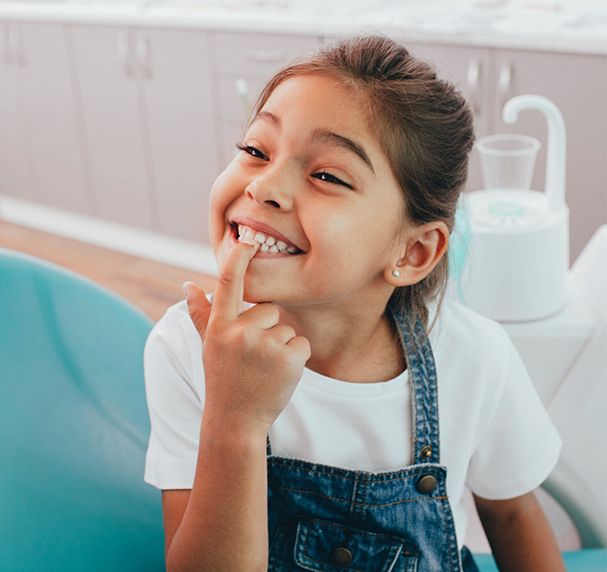 Little girl in dental chair pointing to her smile