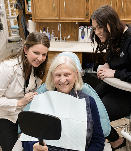 Dental team watching while patient checks smile in mirror