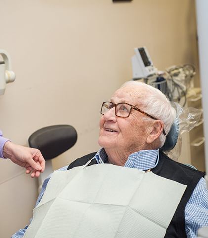 Senior male patient with glasses looking up while sitting in dental chair