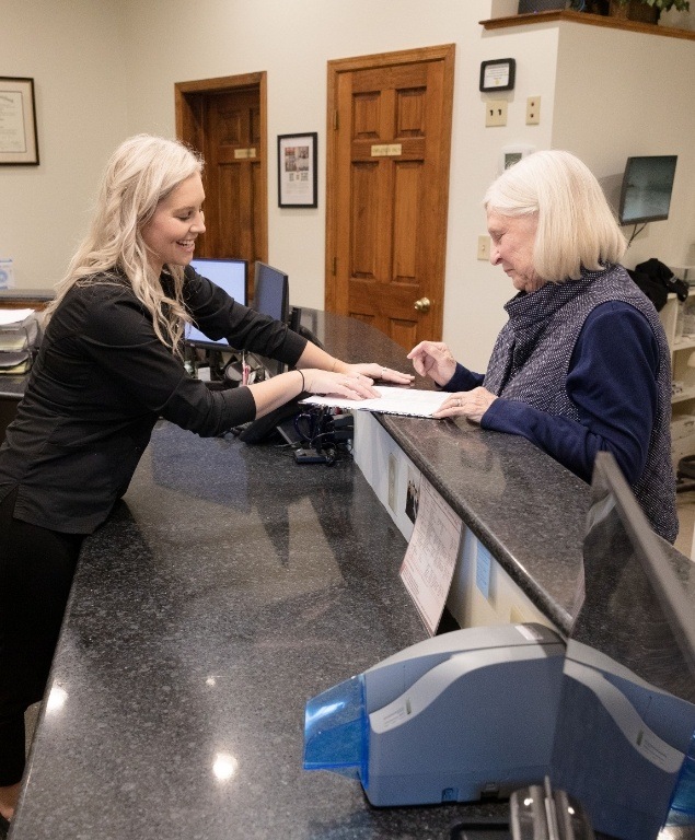 Dental team member at front desk showing a paper to a patient