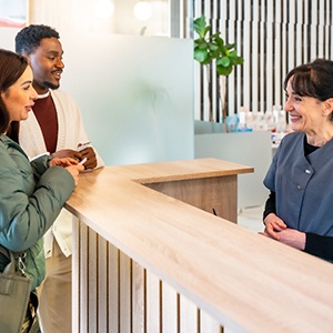 Dental receptionist smiling at couple in lobby