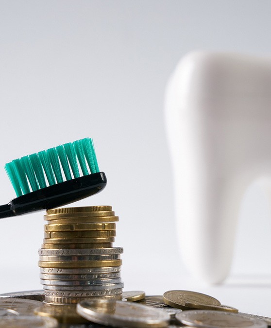 Toothbrush on top of coins with model of tooth in background