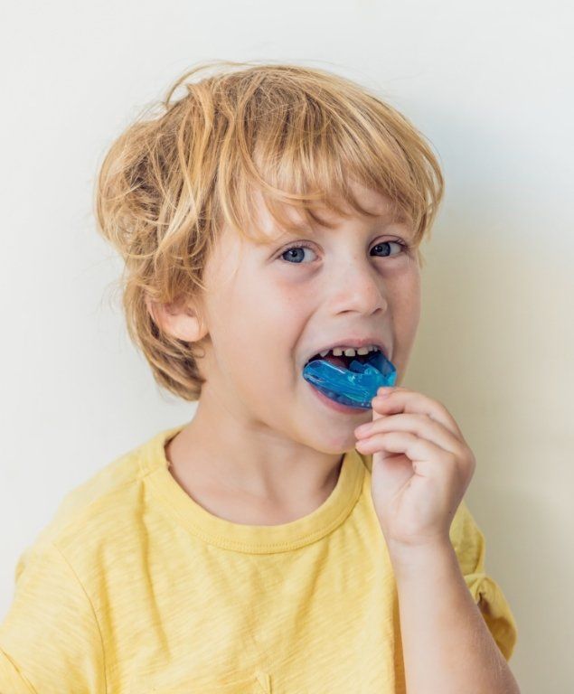 Young boy putting a blue athletic mouthguard over his teeth