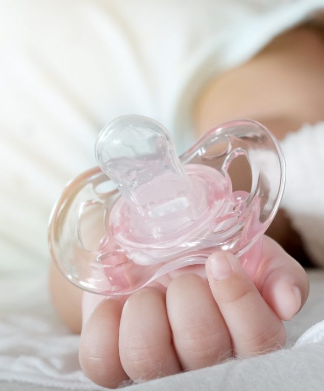 Close up of baby holding a pink pacifier