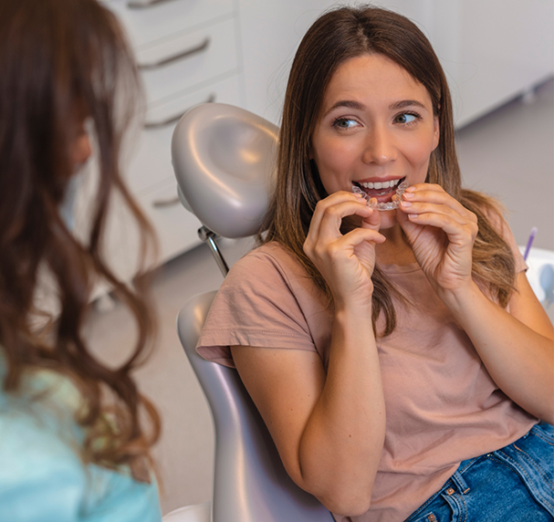 Woman sitting back in dental chair putting in a Spark Clear aligner