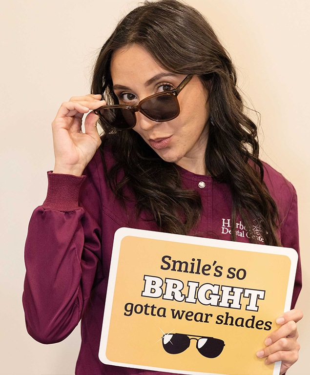 Lilia with sunglasses holding sign that reads smiles so bright gotta wear shades